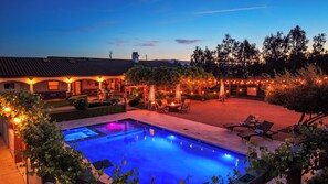 A swimming pool with a patio area, outdoor seating, and string lights.