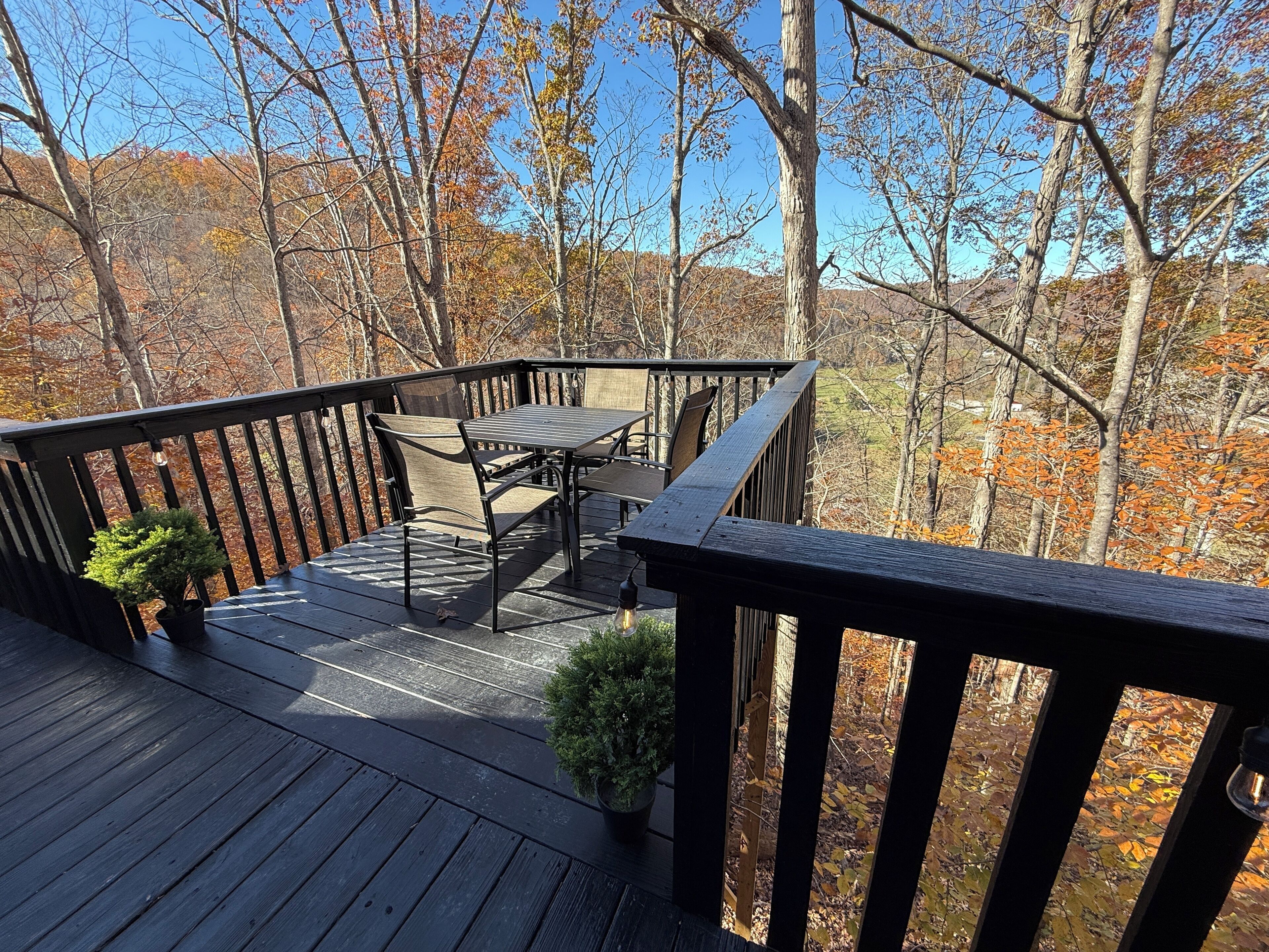 A wooden deck with a table and chairs, surrounded by trees with autumn foliage.