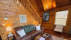Interior acogedor de una cabaña con una escalera de madera, un sofá de cuero marrón, una mesa de centro de madera y una silla.