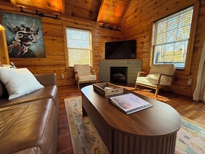 Ein gemütliches Blockhaus-Interieur mit Kamin, Ledersofa und zwei Sesseln.