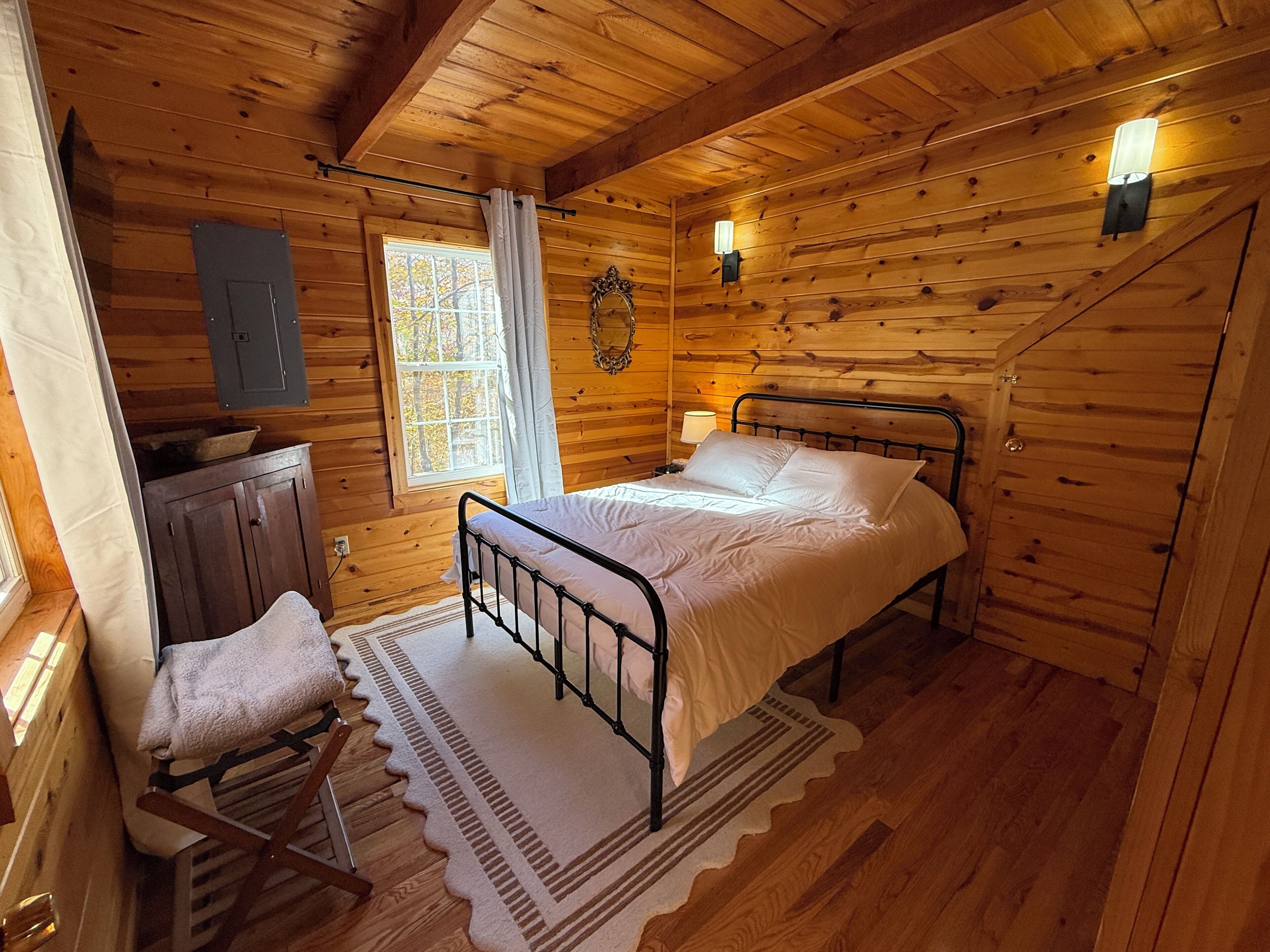 Ein Schlafzimmer einer Holzhütte mit einem Bett, einem Nachttisch, einem Stuhl und einem Fenster.