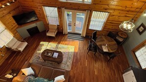 Interior acogedor de una cabaña con suelo de madera, un sofá, una mesa de centro, un televisor y un comedor.