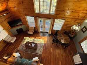 Ein gemütliches Blockhaushaus-Interieur mit Holzboden, einer Couch, einem Couchtisch, einem Fernseher und einem Essbereich.