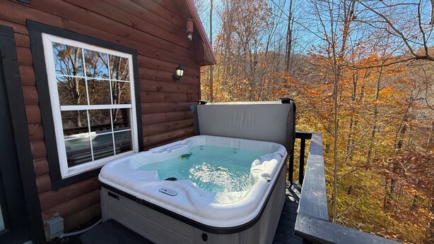 Una cabaña de madera con un jacuzzi en una terraza, rodeada de follaje otoñal.