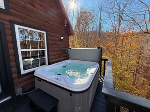 En træhytte med jacuzzi på en terrasse, omgivet af efterårsblade.