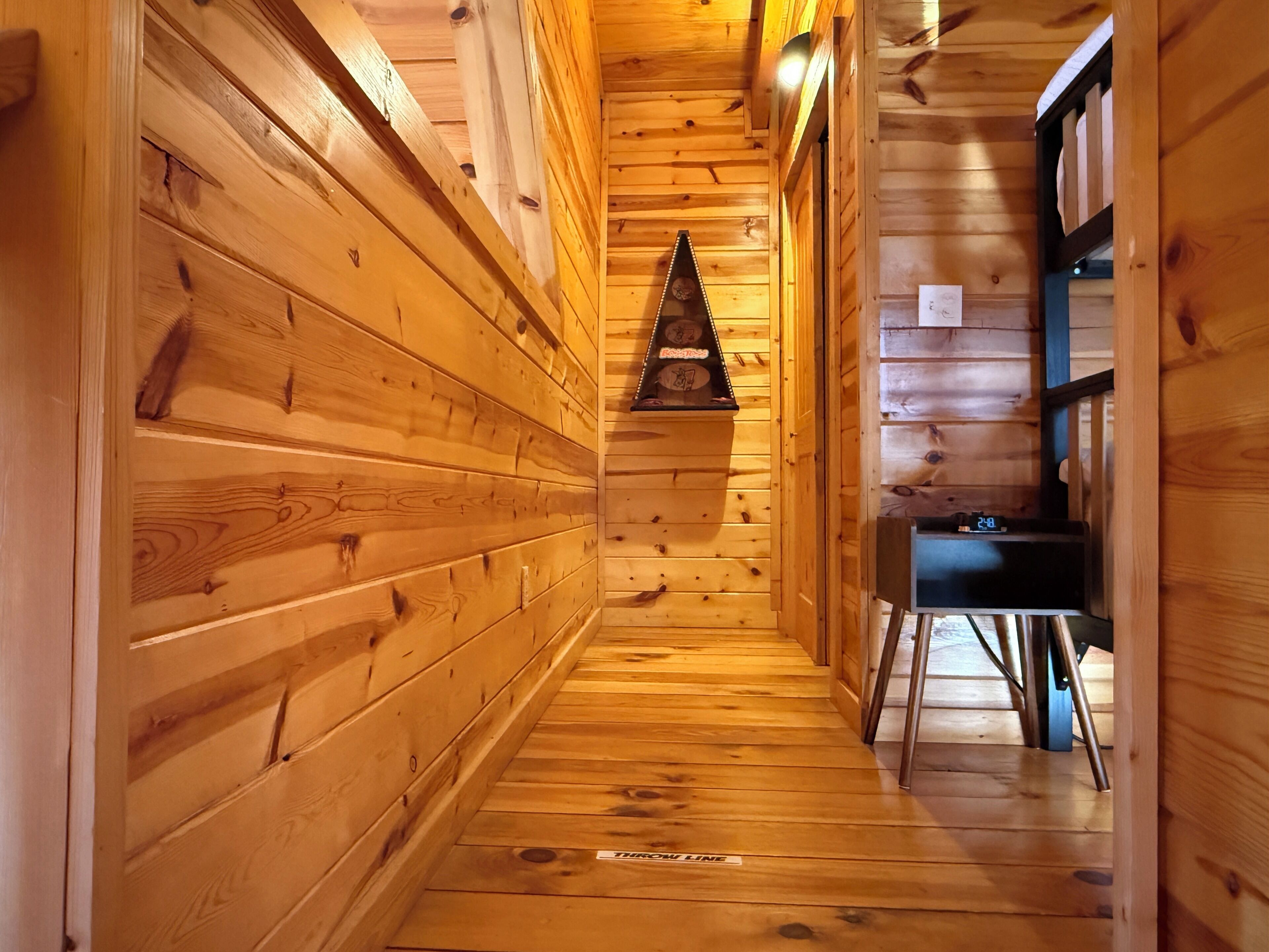 Un couloir intérieur en bois, avec une horloge et une petite table sur laquelle se trouve une autre horloge.