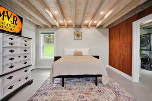 A bedroom with a bed, dresser, and a laundry area.