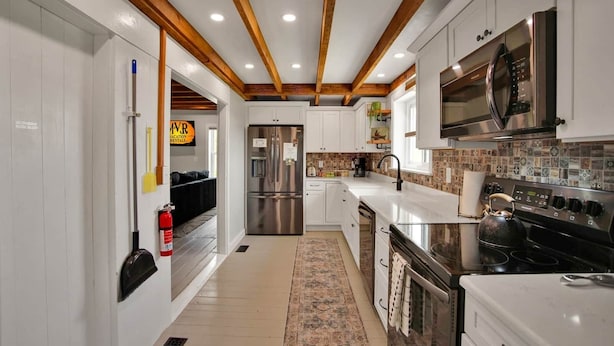A modern kitchen with white cabinets, a stainless steel refrigerator, a microwave, and a stove. - Raven Feather Retreat : Pet Friendly! (Liberty Township)