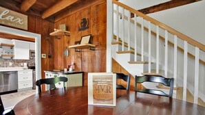 A wooden interior with a dining table, chairs, a framed sign, and a staircase. - Raven Feather Retreat : Pet Friendly! (Liberty Township)