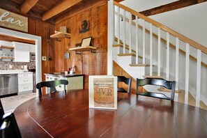 A wooden interior with a dining table, chairs, a framed sign, and a staircase.
