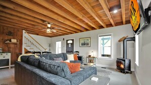 A living room with a fireplace, a sofa, a dining area, and a staircase. - Raven Feather Retreat : Pet Friendly! (Liberty Township)