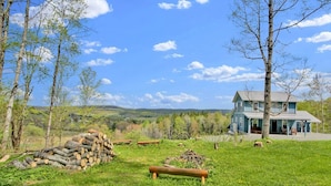 A rustic house with a porch, surrounded by a grassy field and trees. - Raven Feather Retreat : Pet Friendly! (Liberty Township)