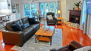A spacious living room with a leather sofa, a wooden coffee table, and a black armchair. There is a fireplace and a television on the right side. The room has large windows and a view of the outdoors. - Pelican’s Point – Weeki Wachee Main River Home with Gulf Access (Weeki Wachee)