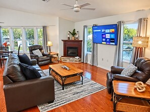A living room with a fireplace, leather sofas, a coffee table, and a flat-screen TV. - Pelican’s Point – Weeki Wachee Main River Home with Gulf Access (Weeki Wachee)
