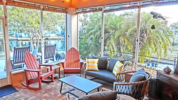 A covered outdoor seating area with wicker furniture, a sofa, and a rocking chair. - Pelican’s Point – Weeki Wachee Main River Home with Gulf Access (Weeki Wachee)