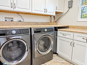 A laundry area with two front-loading washing machines, white cabinets, and a countertop. - Pelican’s Point – Weeki Wachee Main River Home with Gulf Access (Weeki Wachee)