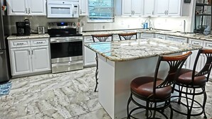 A kitchen with white cabinets, a stainless steel oven, a microwave, and a coffee maker. There is a marble countertop and two bar stools. - Pelican’s Point – Weeki Wachee Main River Home with Gulf Access (Weeki Wachee)