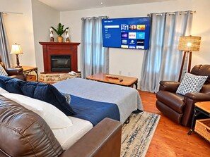 A living room with a fireplace, a flat-screen TV mounted on the wall, a leather sofa, a brown leather armchair, and a wooden coffee table. - Pelican’s Point – Weeki Wachee Main River Home with Gulf Access (Weeki Wachee)