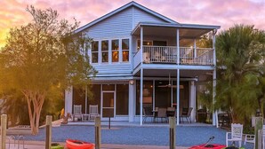 A two-story house with a balcony, a dock with kayaks, and a body of water in the foreground. - Pelican’s Point – Weeki Wachee Main River Home with Gulf Access (Weeki Wachee)