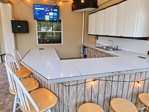 A kitchen with a bar area, white cabinets, and a flat-screen TV mounted on the wall. - Pelican’s Point – Weeki Wachee Main River Home with Gulf Access (Weeki Wachee)