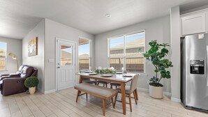 Een moderne keuken met een eethoek, witte kastjes, een roestvrijstalen koelkast en een potplant.