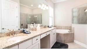 Un baño moderno con encimera de granito, un espejo grande, una bañera y zona de ducha.