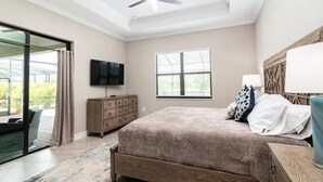 Un dormitorio con una cama grande, un televisor montado en la pared, un tocador de madera y una ventana con persianas.