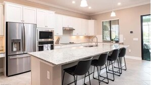 Una cocina moderna con armarios blancos, electrodomésticos de acero inoxidable, encimera de granito y taburetes de bar negros.