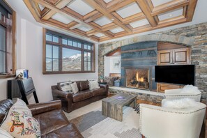 Un salon chaleureux avec une cheminée en pierre, des meubles en cuir et une grande fenêtre donnant sur une vue imprenable sur les montagnes.
