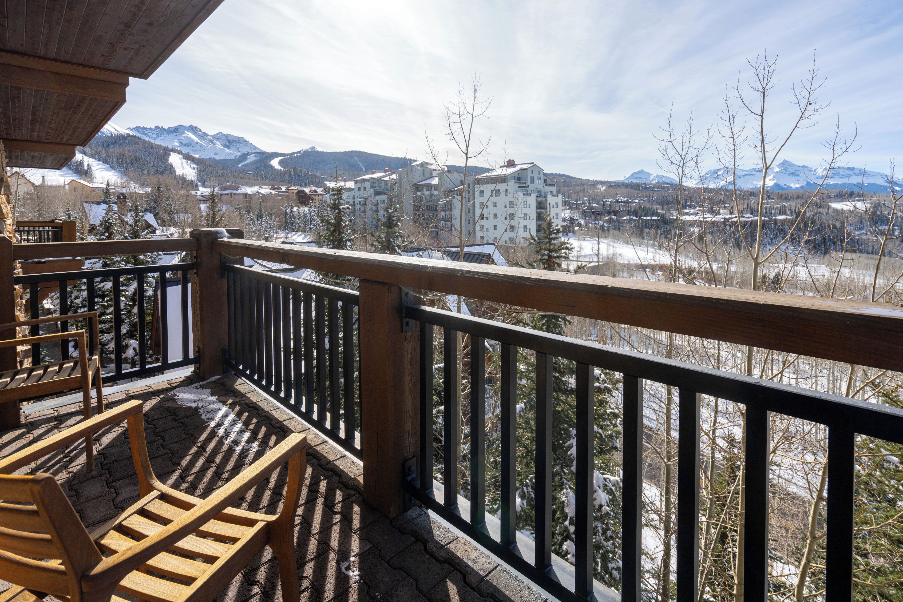 Eine Holzterrasse mit Sitzgelegenheiten im Freien, mit Blick auf eine verschneite Berglandschaft und Gebäude.