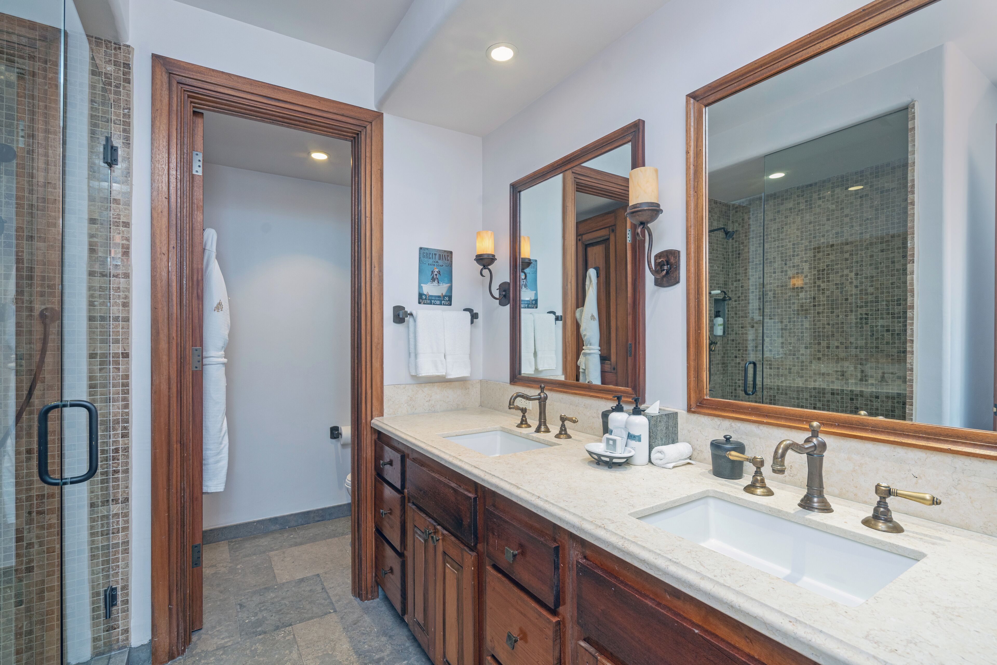 A bathroom with a large mirror, two sinks, wooden cabinets, and a shower area.