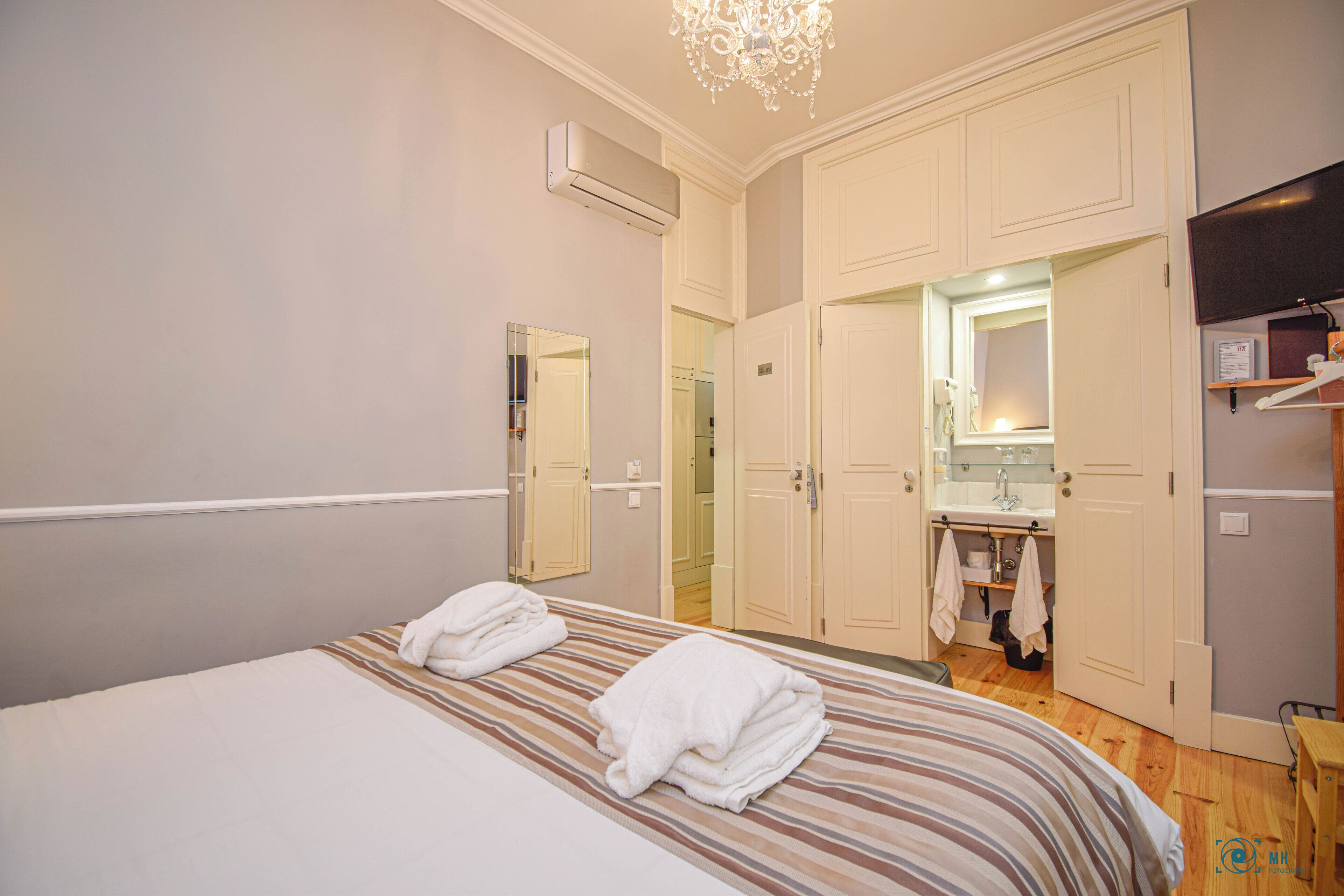Habitación de hotel con una cama, dos toallas, un espejo, un lavabo y un televisor.