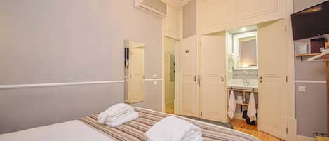 Habitación de hotel con una cama, dos toallas, un espejo, un lavabo y un televisor.
