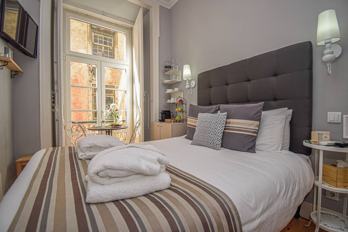 Una cama bien hecha con ropa de cama y toallas a rayas, un cabecero tapizado en gris y una mesita de noche con lámpara.