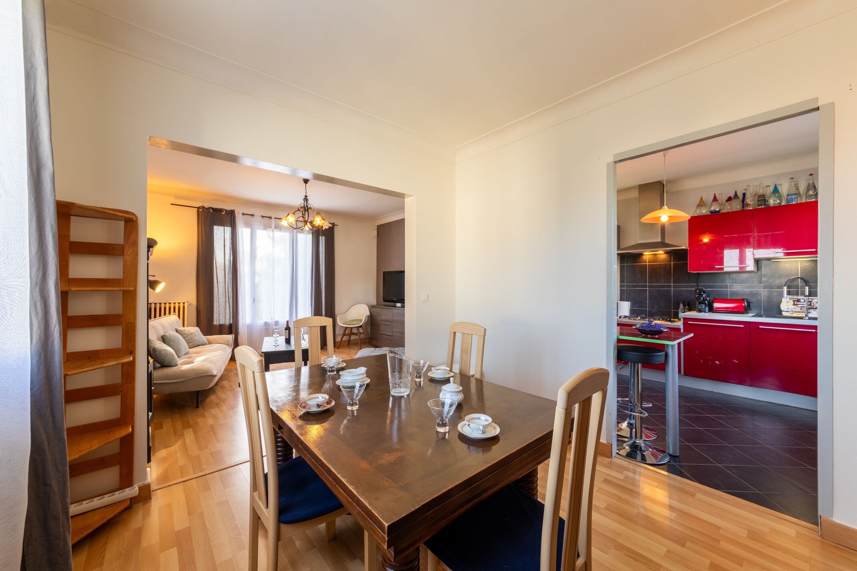 Een eetgedeelte met een houten tafel voor vier personen, een bank en een keuken met rode kastjes.
