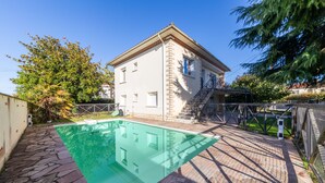 Una casa de dos pisos con piscina, un sendero de piedra y una escalera que lleva al piso superior.