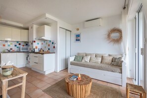 Een moderne woonruimte met een keuken, een witte bank, een ronde houten salontafel, en een eethoek met een houten tafel en stoelen.