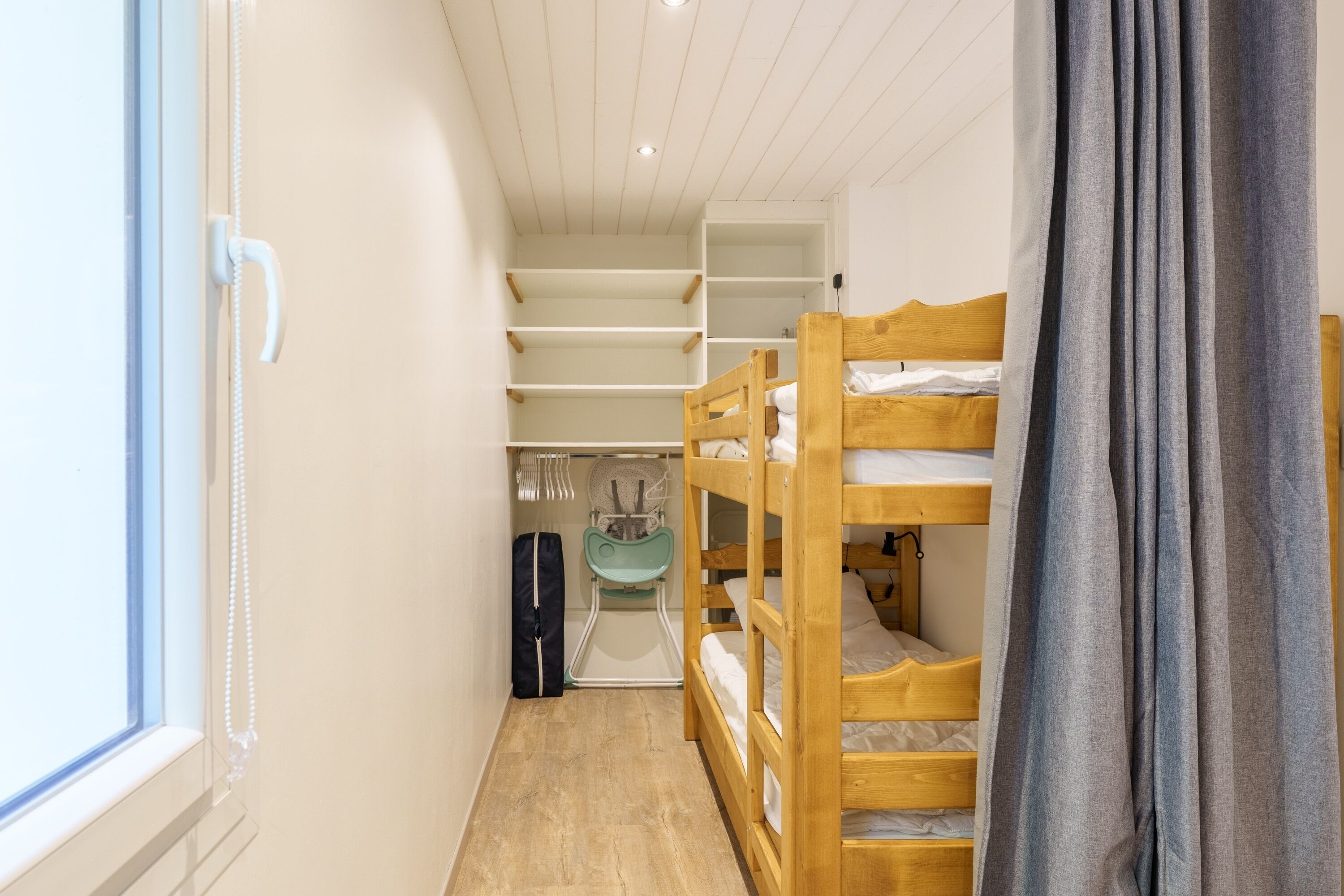 Une chambre avec un lit superposé, une fenêtre, une armoire et un petit coin cuisine.