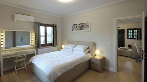 Ein Schlafzimmer mit Bett, Nachttischen, Schreibtisch mit Stuhl, Spiegel mit Beleuchtung und einem Fenster.