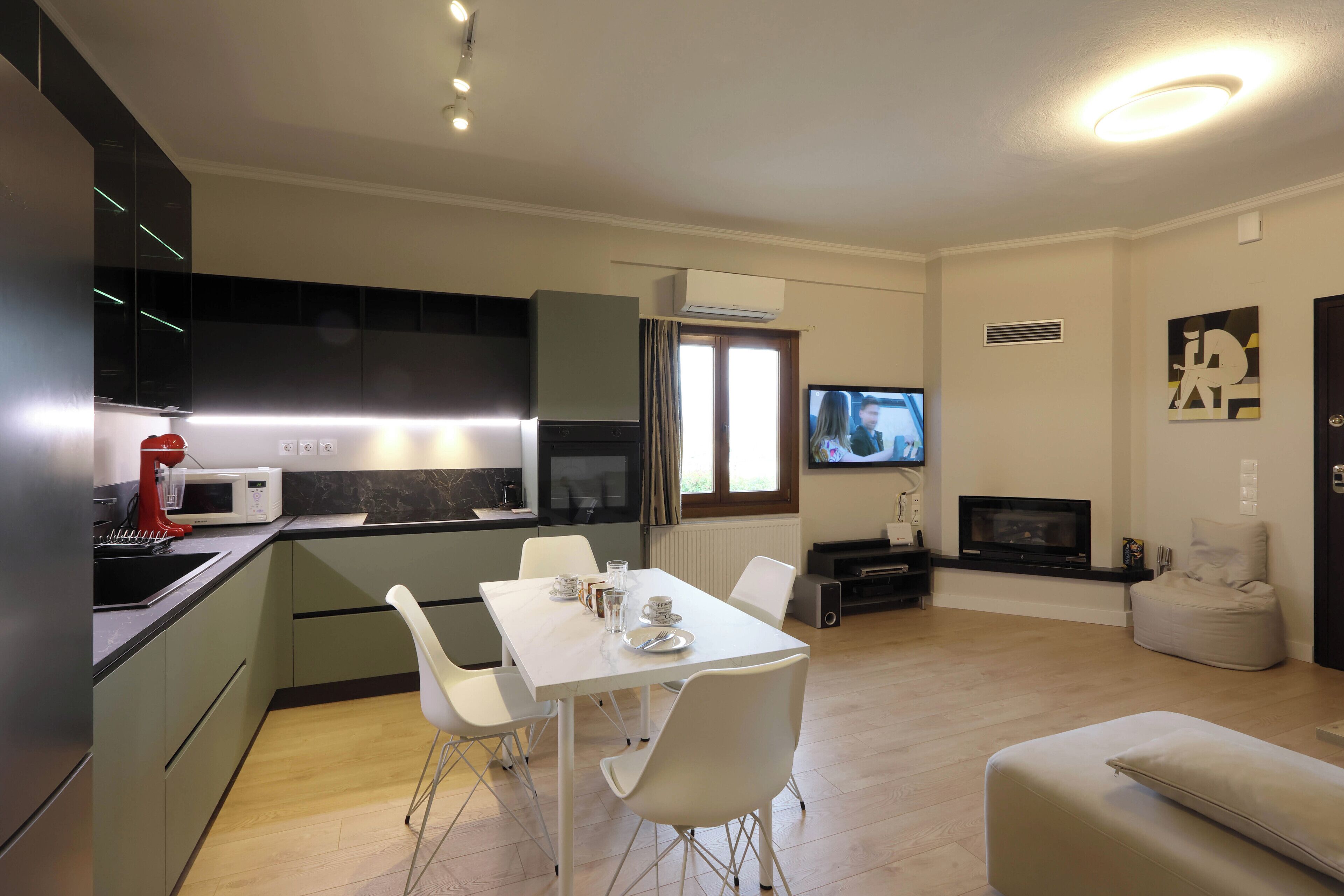 Una cocina moderna con comedor, televisor y zona de estar con sofá y reposapiés.