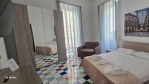 Une chambre d’hôtel avec un lit, une chaise, un miroir et un sol à carreaux aux couleurs vives.