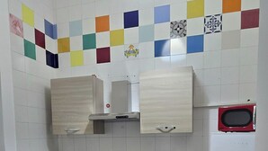 Une cuisine compacte avec une table et des chaises en bois, un four à micro-ondes, un réfrigérateur et un plan de travail coloré recouvert de carreaux.