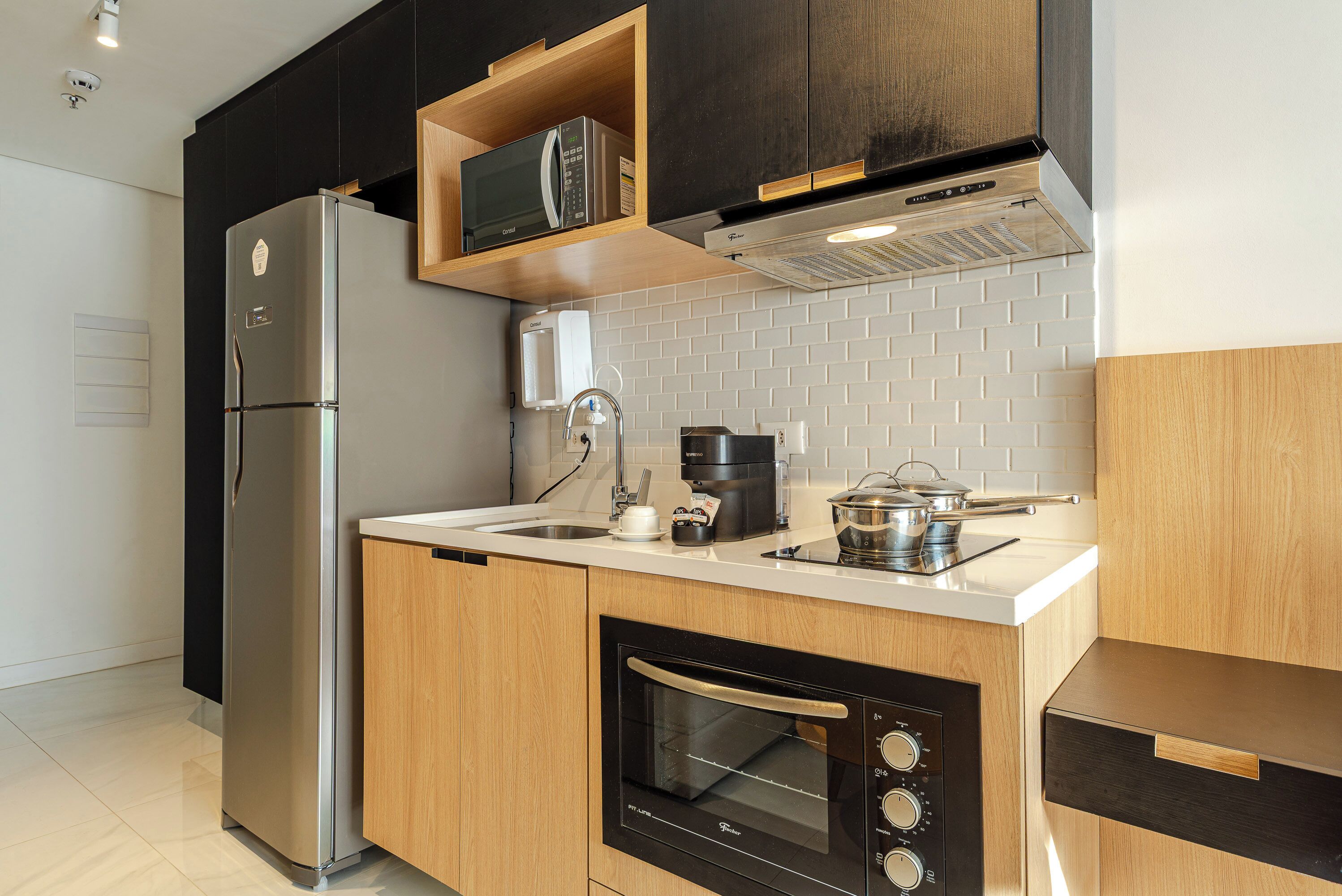 A modern kitchen with a stainless steel refrigerator, built-in oven, microwave, and coffee maker.