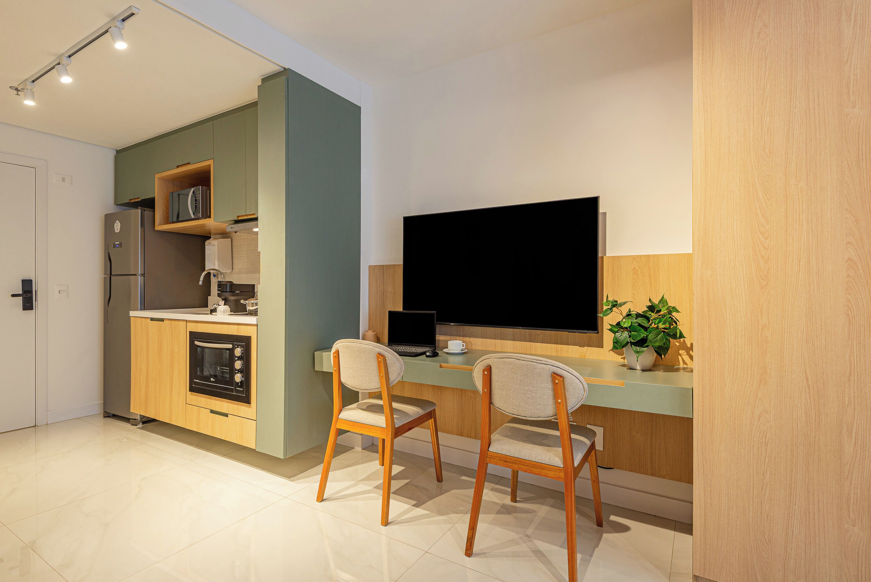 A modern kitchen with a built-in oven, a refrigerator, and a dining area with two chairs and a table.