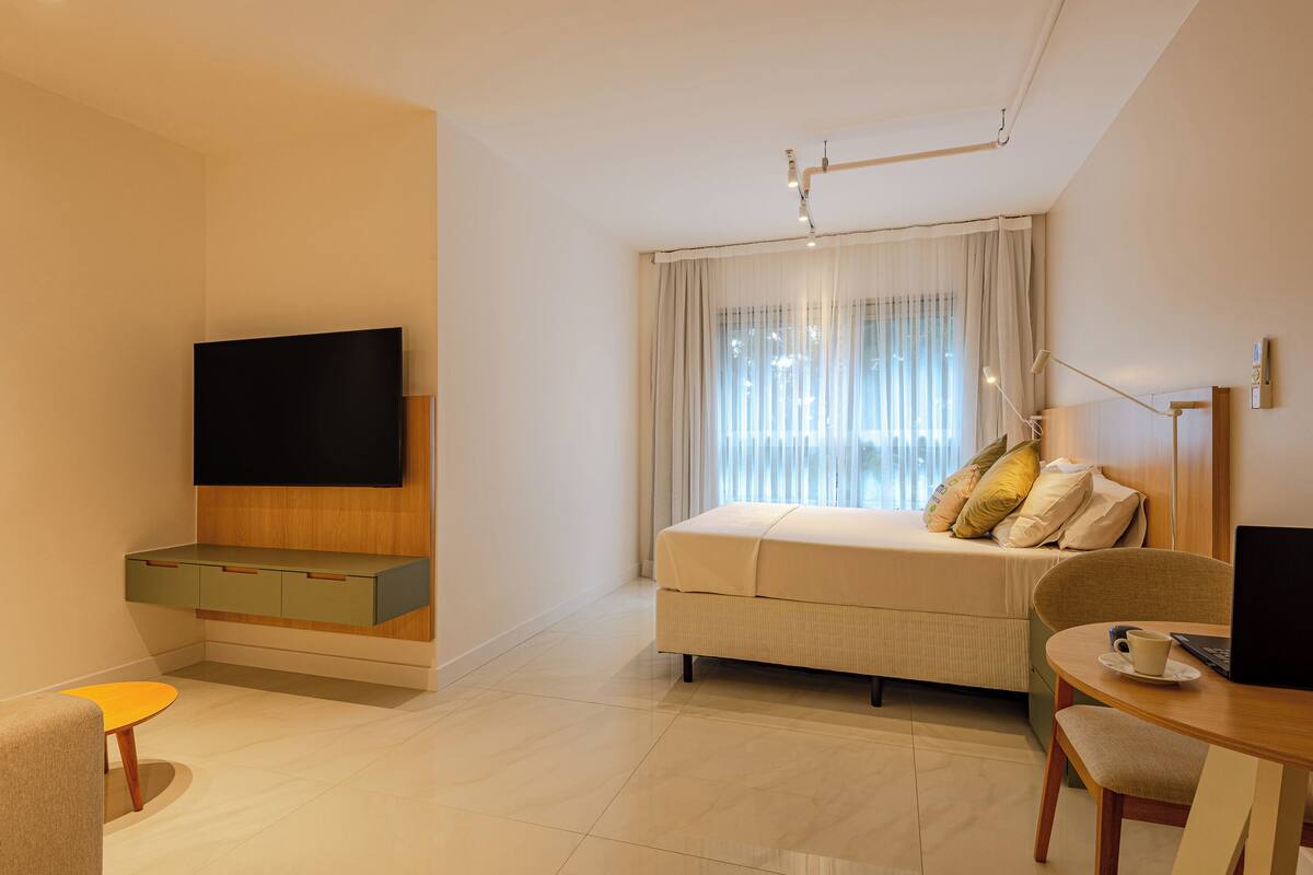 Habitació d'hotel moderna amb televisió de pantalla plana, sofà-llit, taula de dinar i escriptori amb un portàtil.
