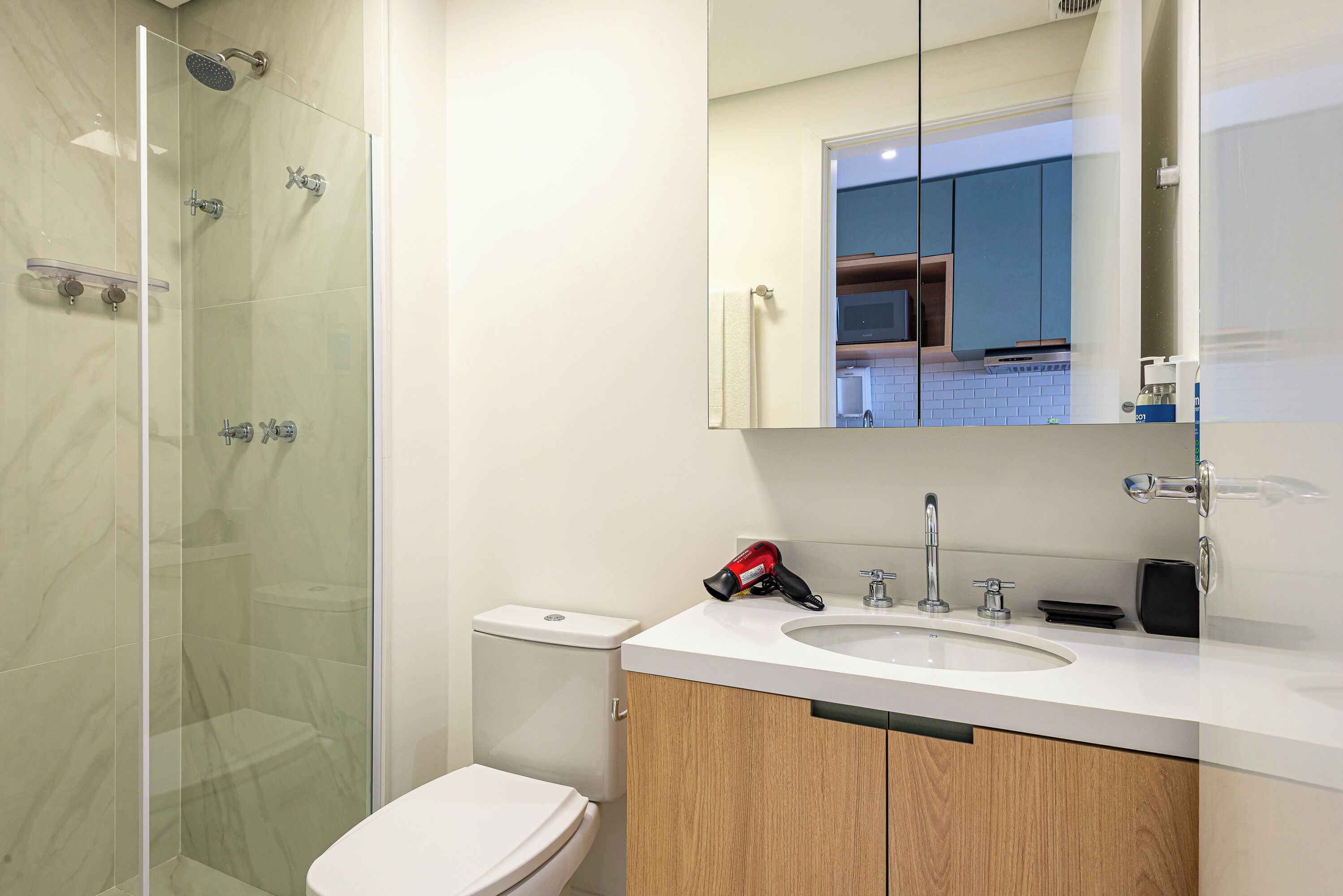 Un baño moderno con ducha de vidrio, inodoro y lavamanos con espejo.