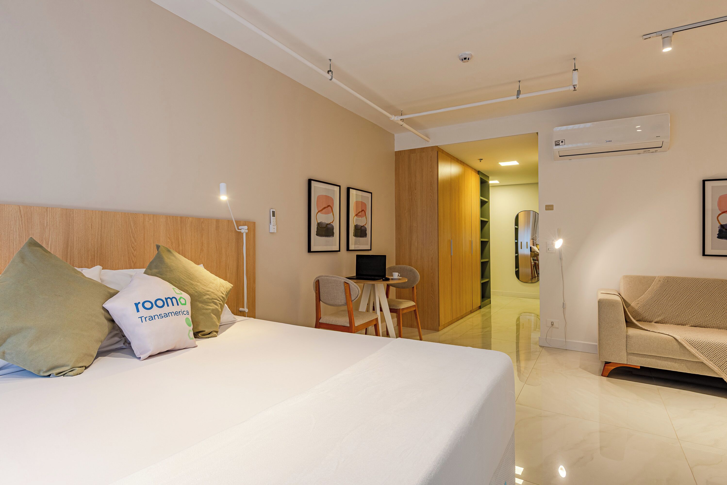 Quarto de hotel com uma cama, uma escrivaninha com um laptop, uma cadeira e um sofá.