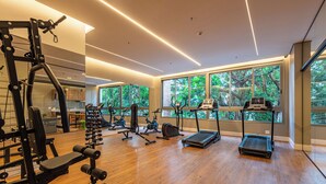 Una palestra moderna con diverse attrezzature per esercizi, ampie finestre che offrono vista su alberi e un pavimento in legno.
