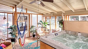 A spa area with a hot tub, wooden flooring, large windows, and various plants.