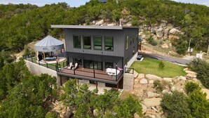 Et moderne hus i to etager med en terrasse, store vinduer og udsigt til en bakket klippeskrab